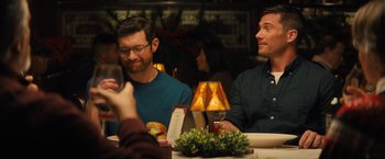 Movie still from “Bros” (2022), directed by Nicholas Stoller – Two men are sitting at a table and one of them is taking a picture; Medium shot, Over the shoulder angle