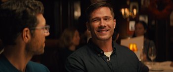 Movie still from “Bros” (2022), directed by Nicholas Stoller – A man smiling for the camera in front of a group of people; Close Up shot, Over the shoulder angle