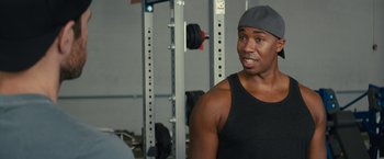 Movie still from “Bros” (2022), directed by Nicholas Stoller – A man in a black tank top is in a gym; Close Up shot, Over the shoulder angle