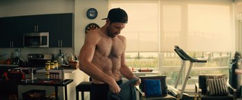 Movie still from “Bros” (2022), directed by Nicholas Stoller – A shirtless man in a hat is holding a towel in a room; Medium shot, Over the shoulder angle