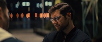 Movie still from “Bros” (2022), directed by Nicholas Stoller – A person wearing glasses and a black jacket; Close Up shot, Over the shoulder angle