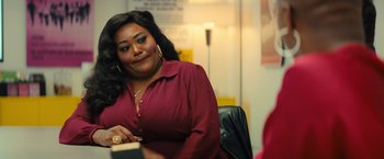 Movie still from “Bros” (2022), directed by Nicholas Stoller – A woman sitting in a chair holding a book; Close Up shot, Over the shoulder angle