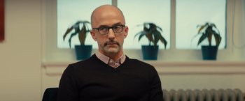 Movie still from “Bros” (2022), directed by Nicholas Stoller – A bald man wearing glasses and a black sweater; Close Up shot, Over the shoulder angle