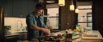 Movie still from “Bros” (2022), directed by Nicholas Stoller – A man in a kitchen preparing food on top of a wooden cutting board; Medium shot, Low angle