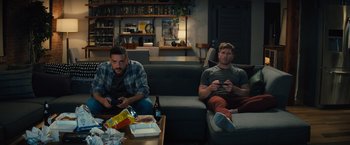 Movie still from “Bros” (2022), directed by Nicholas Stoller – Two men sitting on a couch playing a video game; Wide shot, High angle