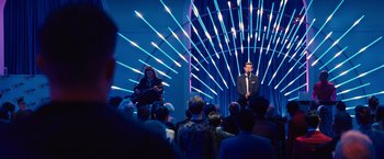 Movie still from “Bros” (2022), directed by Nicholas Stoller – A man and a woman are standing in front of an audience; Extreme Wide shot, Over the shoulder angle