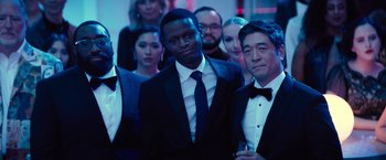 Movie still from “Bros” (2022), directed by Nicholas Stoller – A group of people in suits and ties standing in a room; Medium shot, Over the shoulder angle
