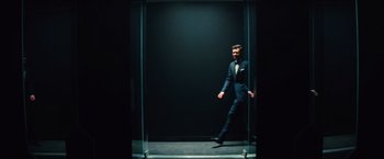 Movie still from “Bros” (2022), directed by Nicholas Stoller – A man in a suit and tie walking through a glass door; Wide shot, Low angle