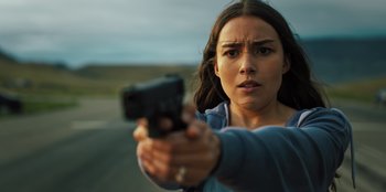A woman holding a gun in front of a road