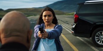 A woman holding a gun in the middle of the road