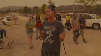 Movie still from “Burning” (2021), directed by Eva Orner – A woman holding a stick while standing in front of a group of people; Medium shot, High angle
