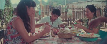 Movie still from “Burning Patience” (2022), directed by Rodrigo Sepúlveda – Two people sitting at a picnic table eating food; Medium shot, High angle