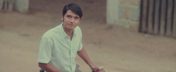 Movie still from “Burning Patience” (2022), directed by Rodrigo Sepúlveda – A young man is sitting on a bicycle; Close Up shot, Over the shoulder angle
