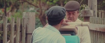 Movie still from “Burning Patience” (2022), directed by Rodrigo Sepúlveda – Two men sitting on a bench looking at each other; Medium shot, Over the shoulder angle