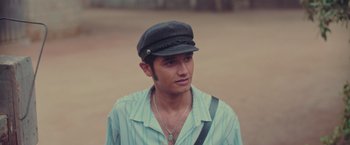 Movie still from “Burning Patience” (2022), directed by Rodrigo Sepúlveda – A man wearing a hat and a necklace; Close Up shot, High angle