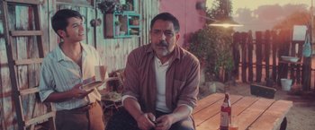 Movie still from “Burning Patience” (2022), directed by Rodrigo Sepúlveda – A man sitting on top of a wooden bench; Medium shot, Over the shoulder angle