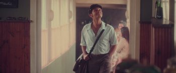 Movie still from “Burning Patience” (2022), directed by Rodrigo Sepúlveda – A man with a hat and a bag walking down a hallway; Medium shot, Low angle