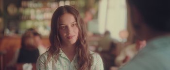 Movie still from “Burning Patience” (2022), directed by Rodrigo Sepúlveda – A woman with long brown hair wearing a green and white striped shirt; Close Up shot, Over the shoulder angle
