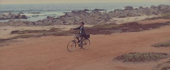 Movie still from “Burning Patience” (2022), directed by Rodrigo Sepúlveda – A man riding a bike on top of a dirt road; Extreme Wide shot, High angle