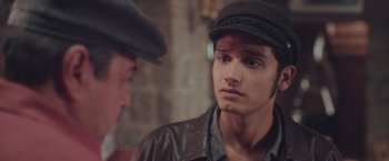 Movie still from “Burning Patience” (2022), directed by Rodrigo Sepúlveda – A man wearing a leather jacket and a hat; Close Up shot, Over the shoulder angle