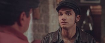 Movie still from “Burning Patience” (2022), directed by Rodrigo Sepúlveda – A man wearing a hat and a leather jacket looking to his left; Close Up shot, Over the shoulder angle