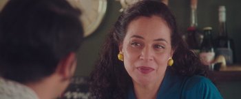 Movie still from “Burning Patience” (2022), directed by Rodrigo Sepúlveda – A person wearing a blue shirt and yellow earrings; Close Up shot, Over the shoulder angle