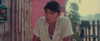 Movie still from “Burning Patience” (2022), directed by Rodrigo Sepúlveda – A young man sitting in front of a pink wall; Close Up shot, Over the shoulder angle