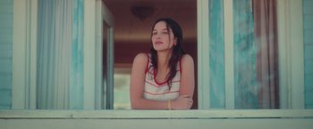 Movie still from “Burning Patience” (2022), directed by Rodrigo Sepúlveda – A woman sitting on a window sill looking out of a window; Medium shot, Low angle