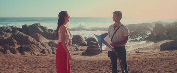 Movie still from “Burning Patience” (2022), directed by Rodrigo Sepúlveda – A man and a woman standing on a beach holding a kite; Wide shot, High angle