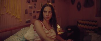 Movie still from “Burning Patience” (2022), directed by Rodrigo Sepúlveda – A woman sitting on a bed in a room; Close Up shot, Over the shoulder angle