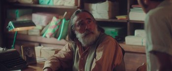 Movie still from “Burning Patience” (2022), directed by Rodrigo Sepúlveda – An older man with long grey hair and a long beard; Close Up shot, Over the shoulder angle