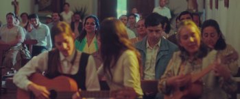 Movie still from “Burning Patience” (2022), directed by Rodrigo Sepúlveda – A group of people sitting in a room; Medium shot, Over the shoulder angle