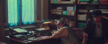 Movie still from “Burning Patience” (2022), directed by Rodrigo Sepúlveda – An older man sitting at a desk with a typewriter; Medium shot, High angle