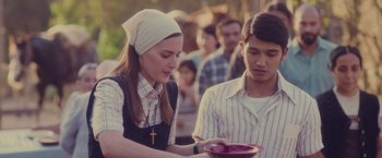 Movie still from “Burning Patience” (2022), directed by Rodrigo Sepúlveda – A woman holding a plate in front of a man; Medium shot, Over the shoulder angle