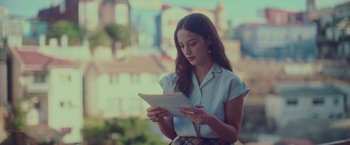 Movie still from “Burning Patience” (2022), directed by Rodrigo Sepúlveda – A woman is looking at a piece of paper; Medium shot, Over the shoulder angle
