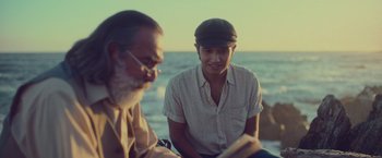 Movie still from “Burning Patience” (2022), directed by Rodrigo Sepúlveda – A man sitting next to another man on the beach; Close Up shot, Over the shoulder angle