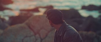 Movie still from “Burning Patience” (2022), directed by Rodrigo Sepúlveda – A man wearing a hat looking out at the ocean; Close Up shot, High angle