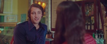 Movie still from “Burning Patience” (2022), directed by Rodrigo Sepúlveda – A man sitting in front of a woman in front of a mirror; Medium shot, Over the shoulder angle