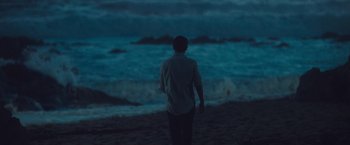 Movie still from “Burning Patience” (2022), directed by Rodrigo Sepúlveda – A man standing on the beach looking at the ocean; Extreme Wide shot, High angle