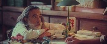 Movie still from “Burning Patience” (2022), directed by Rodrigo Sepúlveda – An older man sitting at a table with a cup of coffee; Medium shot, Over the shoulder angle