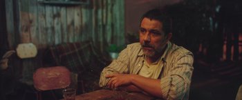 Movie still from “Burning Patience” (2022), directed by Rodrigo Sepúlveda – A man sitting at a table with a glass of wine; Medium shot, Over the shoulder angle