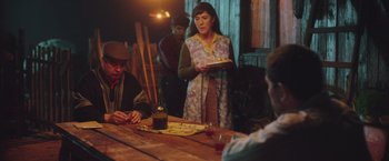 Movie still from “Burning Patience” (2022), directed by Rodrigo Sepúlveda – A group of people sitting at a wooden table; Medium shot, Over the shoulder angle