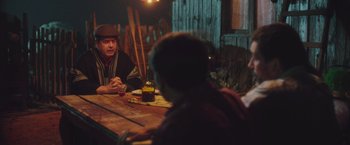 Movie still from “Burning Patience” (2022), directed by Rodrigo Sepúlveda – A group of people sitting at a wooden table; Medium shot, Over the shoulder angle
