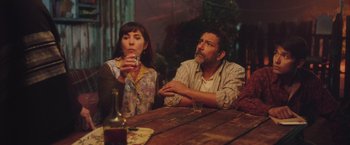 Movie still from “Burning Patience” (2022), directed by Rodrigo Sepúlveda – A man and a woman sitting at a wooden table; Medium shot, Low angle
