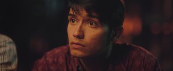 Movie still from “Burning Patience” (2022), directed by Rodrigo Sepúlveda – A person wearing a red shirt; Close Up shot, Over the shoulder angle