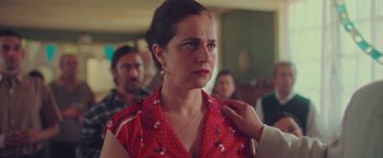 Movie still from “Burning Patience” (2022), directed by Rodrigo Sepúlveda – A woman in a red polka dot shirt is looking down; Medium shot, Over the shoulder angle