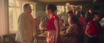 Movie still from “Burning Patience” (2022), directed by Rodrigo Sepúlveda – A man and a woman shaking hands in front of a group of people; Medium shot, Over the shoulder angle