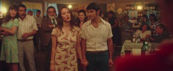 Movie still from “Burning Patience” (2022), directed by Rodrigo Sepúlveda – A man and a woman holding hands while standing in a room; Medium shot, Over the shoulder angle