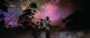 A man sitting on top of a brick wall with fireworks in the background
