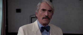 An older man wearing a white suit and a blue bow tie